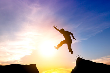 Silhouette of man jumping through the gap on sunset background.challenge for across barrier to achievement or successful in business concept