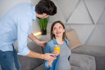 Dark-haired man giving a glass of orange juice to his pregnant wife