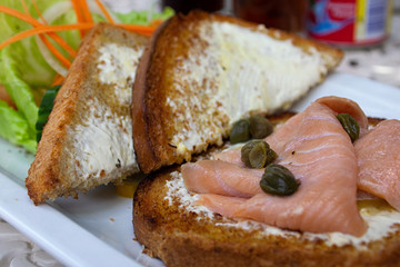 Toast with salmon, cream cheese and capers.  Taken at a lower angle.