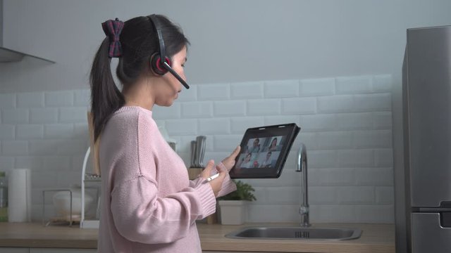 Business woman wear headset and talking about work in video conference at kitchen. Asian team using tablet online meeting in video call.Working from home, Working remotely and Self isolation at home