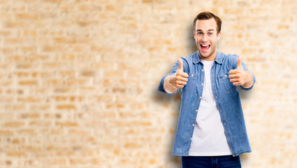 Happy excited man shout and showing thumbs up gesture, in blue smart casual wear, standing again loft style wall background. Emotions and success concept picture.