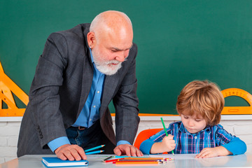 Senior teacher with pupil at back of classroom at the elementary school. Child at school lesson...