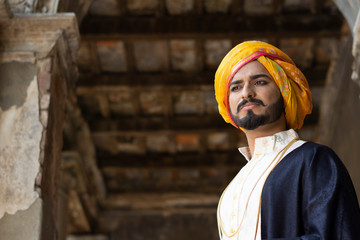 Low angle portrait of a young Indian man with ethnic wear with turban in an old vintage house....