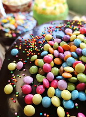 chocolate fudge cake closeup, covered with colourful mini smarties, more cakes in the background