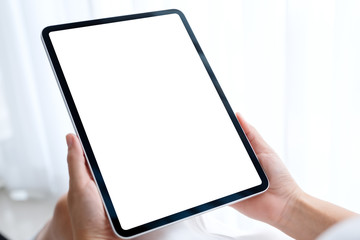 Mockup image of a woman holding black tablet pc with blank white desktop screen while sitting in bedroom with feeling relaxed in the morning
