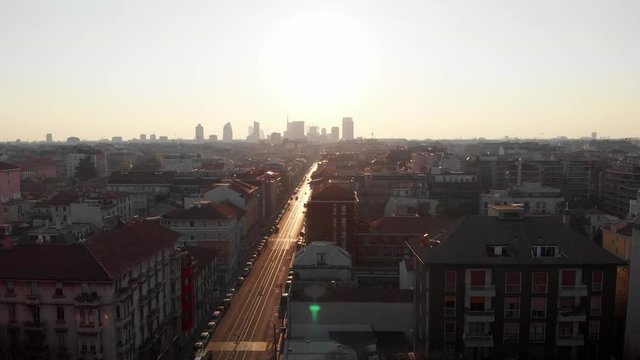 Drone aerial view of Milan skyline from above against bright sun over the city. Shot in Lambrate area during Coronavirus lockdown quarantine. Moving sideways over main street.