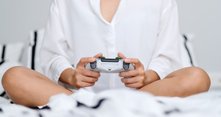 Closeup image of a woman holding game controller while playing games , sitting on a white cozy bed at home