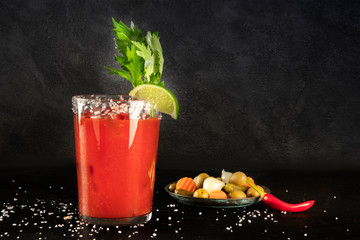 Bloody Mary cocktail with tomato juice, lime, and celery, wiuth pickles and a chili pepper, side view on a black background with copy space © laplateresca