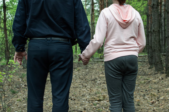 A man holds the hand of a teenage girl in the woods. The concept of kidnapping and child trafficking.