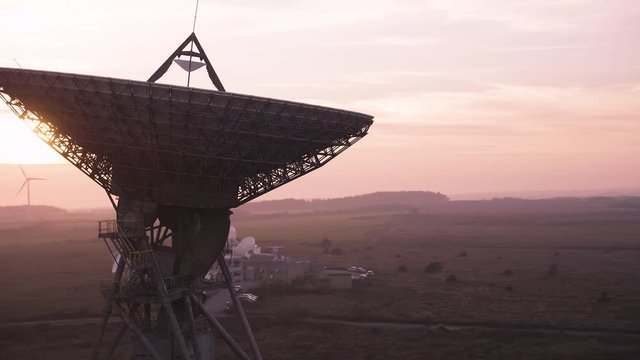Cinematic aerial of a massive satellite dish searching space for new discoveries. Purple moody dusk environment