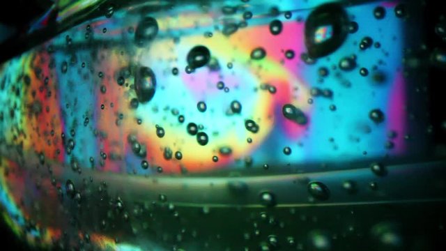 Abstract background - pulling back from back lit hand sanitizer bottle on its side. Background colors changing four times to show great detail inside the hand sanitizer bottle; lots of air bubbles.
