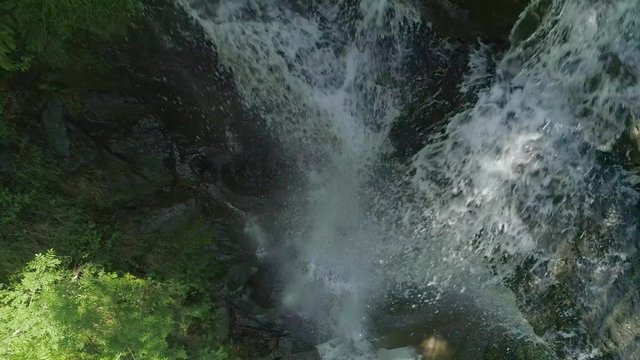 The top-down view of a waterfall located in Spain in the Gorbea Natural Park. From a birds-eye view, you can see the water crashing down over the rocks into the depth surrounded by the green foliage.