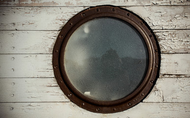 Round window on board the ship. Luke. Old wood texture, white. Reflection in the glass. Metal frame. Detail.
