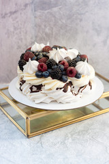 Meringue cake Pavlova with fresh ripe raspberry and blueberry, and whipped cream on grey background.
