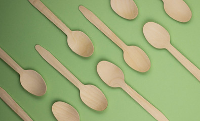 Eco-friendly disposable tableware made of bamboo wood and paper on a green background. Draped spoons scattered on the table. The concept of zero waste. Preserving the purity of nature