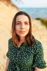 Close-up portrait of young beautiful girl outdoors. A brunette girl in green polka dress is looking at the camera