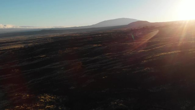 sunrise over old lava flow in Kona Hawaii, drone shot pan right Mauna Kea silhouette