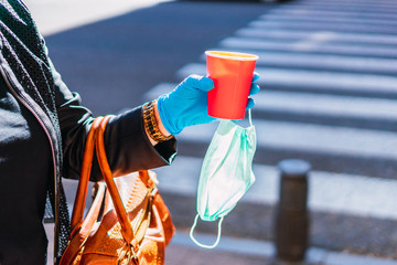 Drinking coffee in the street with mask.
woman on the street, holding coffee and a mask for coronavirus