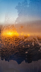 The light of the setting sun through the frosty pattern on the glass in winter