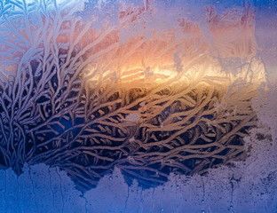 The light of the setting sun through the frosty pattern on the glass in winter