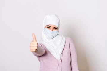 Muslim Woman with protective mask showing thumb up. Woman with face mask in hijab, protection of Coronavirus in human lungs. MERS-CoV, SARS, Adenoviruses and other respiratory viruses