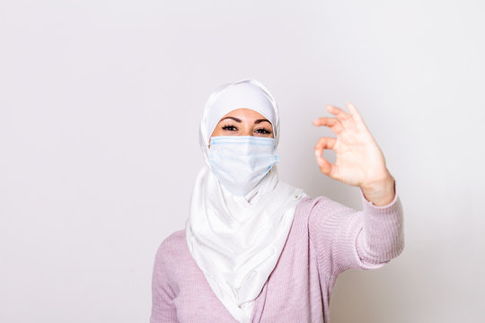 Young muslim woman wearing medical face mask, studio portrait. Woman with hijab Wearing Protective Mask and Showing OK sign. Woman wearing surgical mask for corona virus