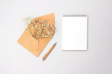 Beautiful vintage flat lay minimal composition with wooden pen, notebook and brown kraft paper envelope with gypsophila Baby's-breath flowers on grey background with copy space for your text