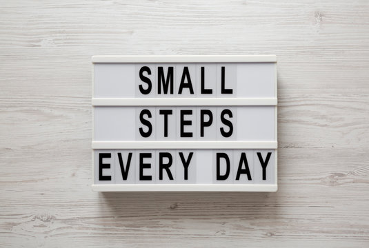 'Small steps every day' words on a lightbox on a white wooden background, top view. Overhead, from above, flat lay.
