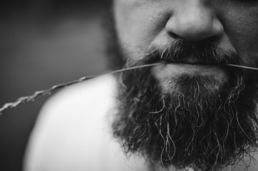 Cropped portrait of a bearded brunette man with a straw in his mouth. Close up, Black and white photo. selective focus