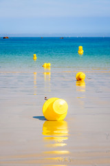 Five large yellow buoys lying on the wet sand and floating on the sea, delimiting a launching channel for small boats on the beach in Penvenan, Brittany, France, under a bright sunshine.