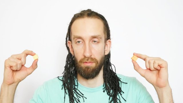 A young beautiful braids man makes a choice and eats two fruit candies against white background