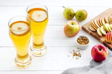Glasses of beer with apple and peer on white wooden desk