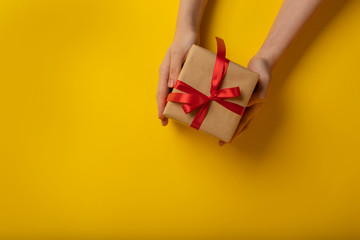 Flat lay of female hands holding handmade present on yellow background
