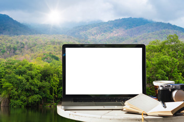 Fototapeta premium Mockup of laptop computer with empty screen with camera,notebook,coffee cup on table at landscape lake views nature forest Mountain views spring with white cloud background,Freelance work and holiday