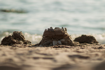 Sand castle on the beach with pebbles.