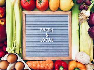 Fresh and Local sign against a colorful background of fresh fruit and vegetables. Farmers market ingredients. Locally sourced, organic and healthy veggies. Concept message board flat lay