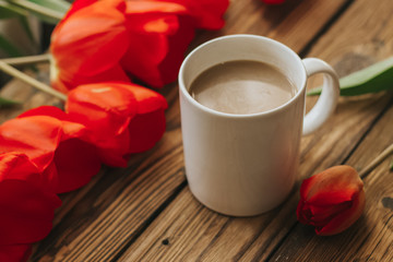 Fototapeta na wymiar Morning concept with white cup of coffee, red tulips, laptop Wooden background. Work from home. Free copy space for text