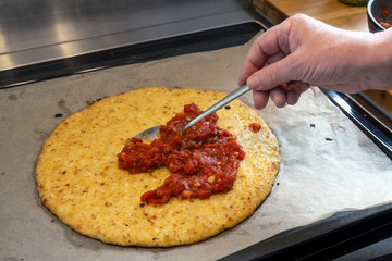 Hand is spreading tomato sauce on a pizza crust from shredded cauliflower, cooking a healthy...