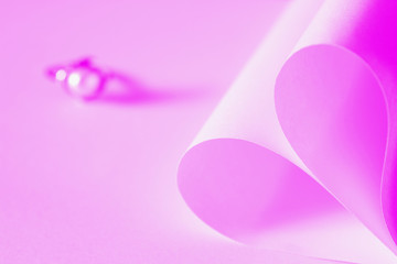 Heart shaped origami paper and pearl ring on pink background.