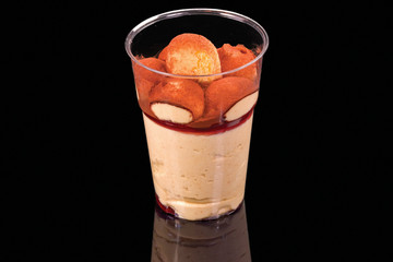 Tasty dessert tiramisu cake in a cup, isolated on black background, with reflection