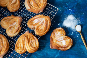 Homemade sugar buns on a cooling rack with sugar for sprinkling. Palmiers, elephant ear, puff pastry cookie
