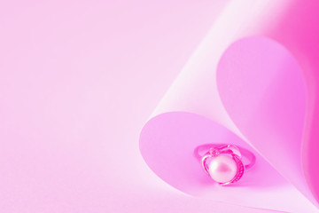 Heart shaped origami paper and pearl ring on pink background.