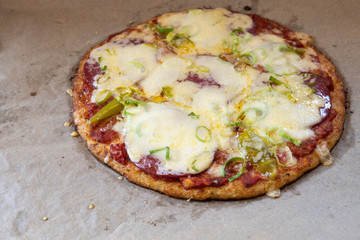 Pizza with cauliflower crust topped with salami, pepperoni, leek and cheese on baking paper,