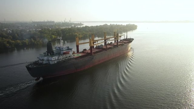 Slowmo aerial cargo bulker with bulk commodities sailing from seaport after loading coarse grain on ship to transfer seaborn trade goods. Logistics vessel on voyage. Merchant cargo with oats dispatch