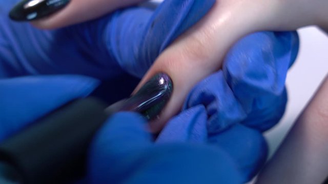 Closeup view video footage of painted female fingernail. Young woman makes modern trendy black naildesign in beauty spa salon. Gel polish with shiny colorful cat eye effect.