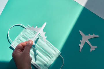 Hand holding paper plane over face mask takes it from shadow to light. Air travel resumes after...