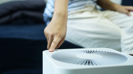 Hand turn on air purifier machine. on the bed room at home, free space.increase in air humidity indoors, comfortable living conditions, Preventing allergies. PM 2.5