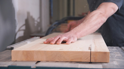 Woodworker works on machine with wooden board. Carpenter saws wood on circular saw machine.