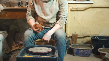 Cropped portrait of craftsman working with loam at kick wheel in pottery workshop. Small business concept.