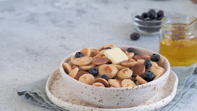Trendy food - pancake cereal. Honey dripping on heap of mini cereal pancakes in boul on gray cement background. Copy space left for text.